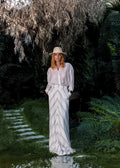 Day One Concept Store cream and beige striped maxi skirt with a fluid, semi-sheer design. Model wears a white shirt and hat.