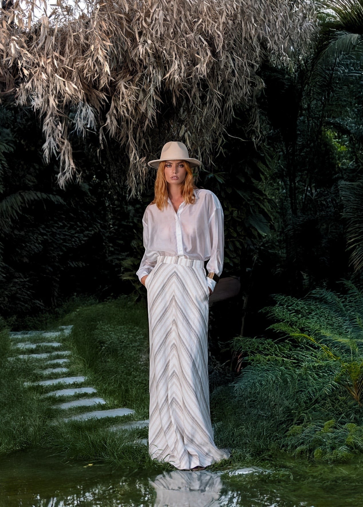 Day One Concept Store cream and beige striped maxi skirt with a fluid, semi-sheer design. Model wears a white shirt and hat.